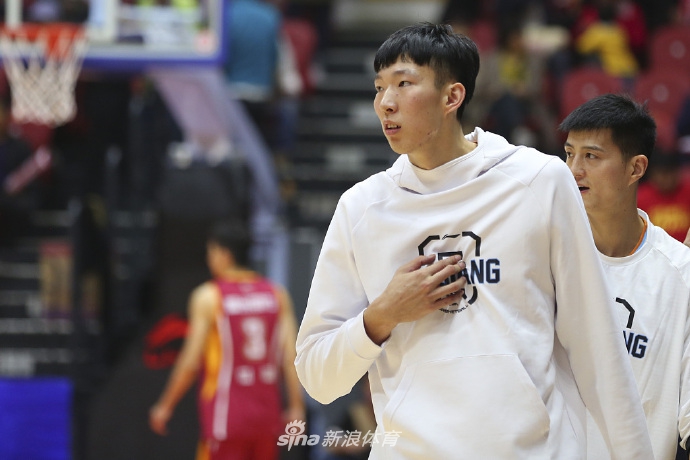 队医蹲在地上全神贯注地检查周琦的左脚踝，周琦则低头凝视，紧锁的眉头透露出他对伤情的担忧