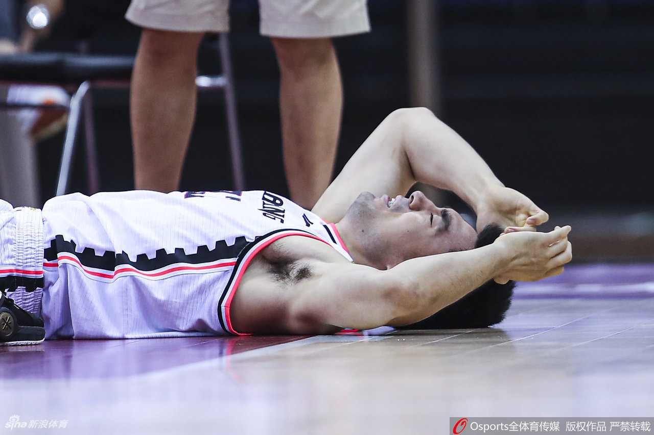 俞长栋在队友的搀扶下单脚跳着离场，他表情痛苦，身后的球馆灯光显得格外刺眼。