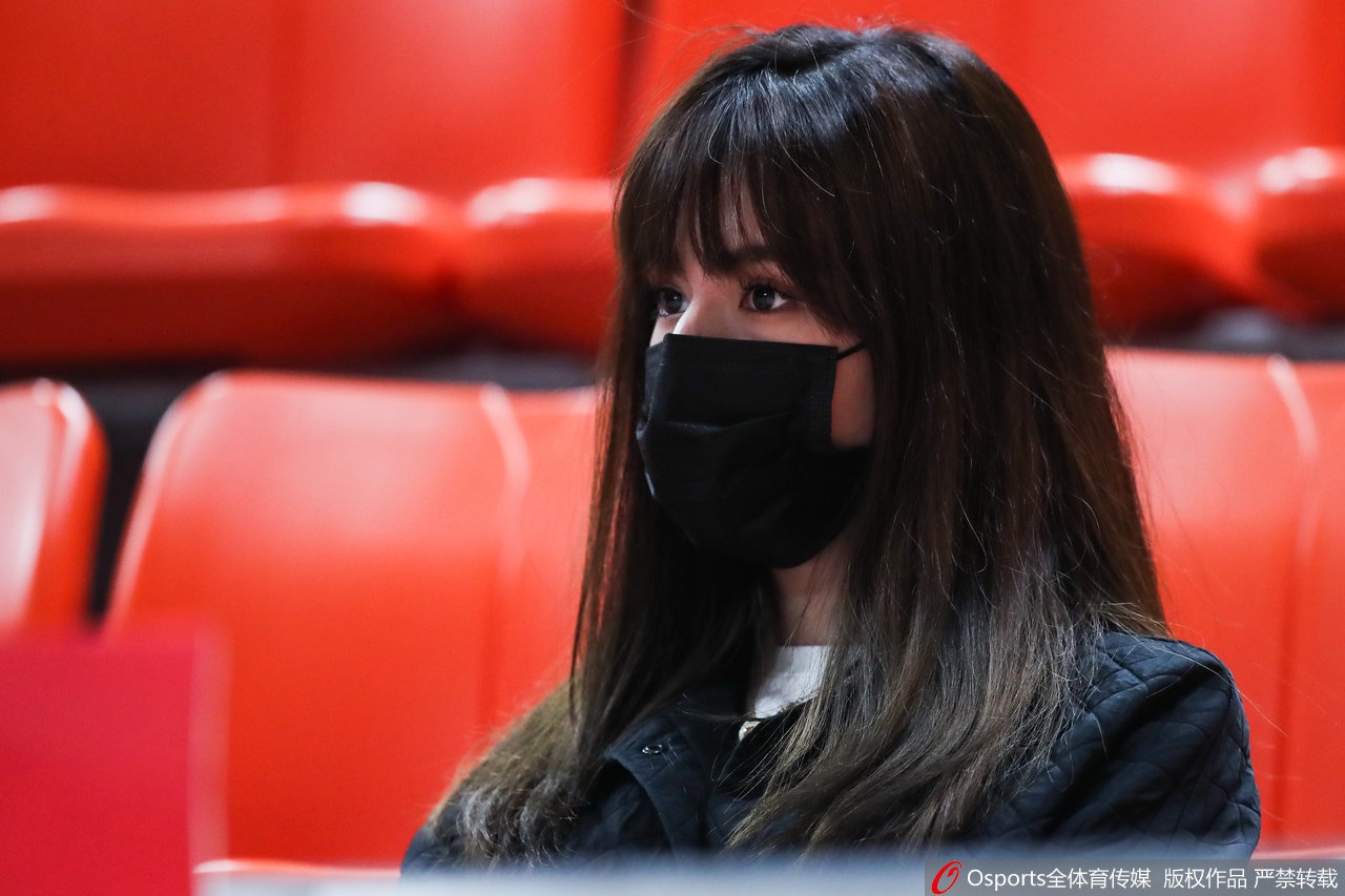 阿迪娜端坐看台，眼神专注地望着赛场方向，即使戴着口罩也难掩其清秀精致的面容，高扎的马尾辫显得活力十足。