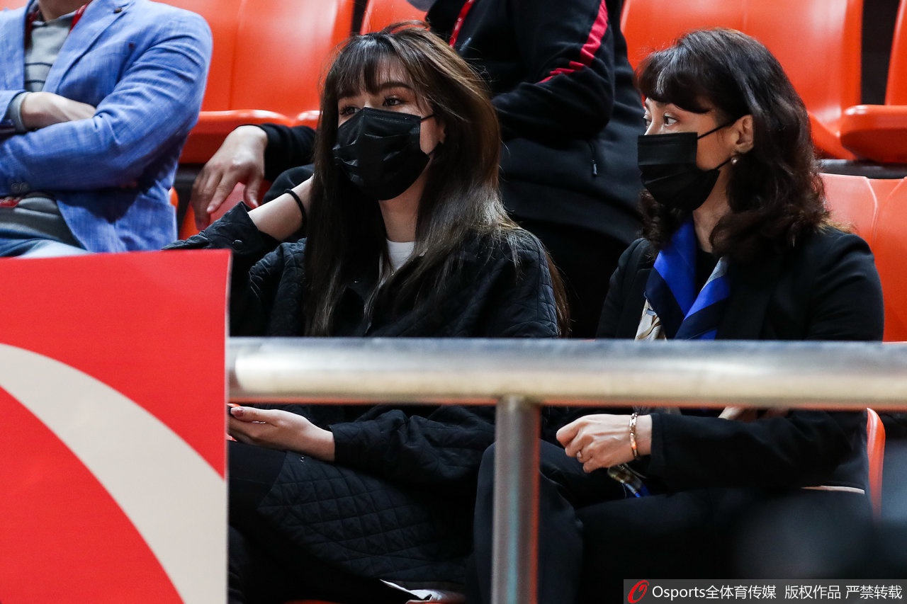 阿迪娜身穿深色外套站立在看台通道，修长的身材一览无余，她正微笑着看向镜头，气质清新脱俗，宛如邻家姐姐般亲切。