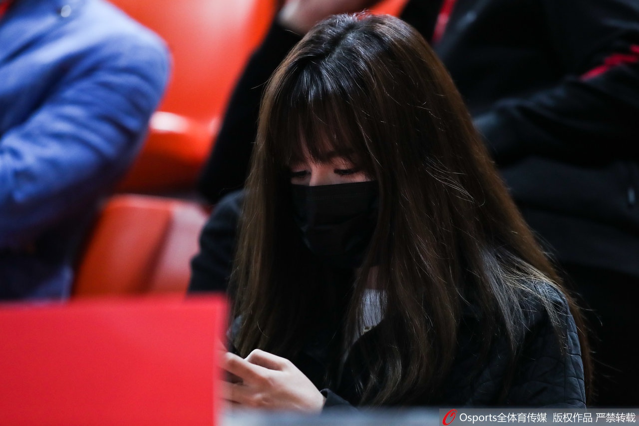 阿迪娜身穿浅色休闲外套，单手托腮凝视赛场，眼神清澈明亮，即便在人群中依然气质出众，仿佛自带光环。