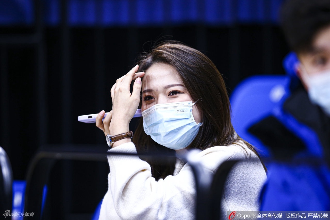 一位戴着黑框眼镜的文艺范女球迷，双手轻托脸颊，眼神中流露出对比赛进程的无限关切与好奇。