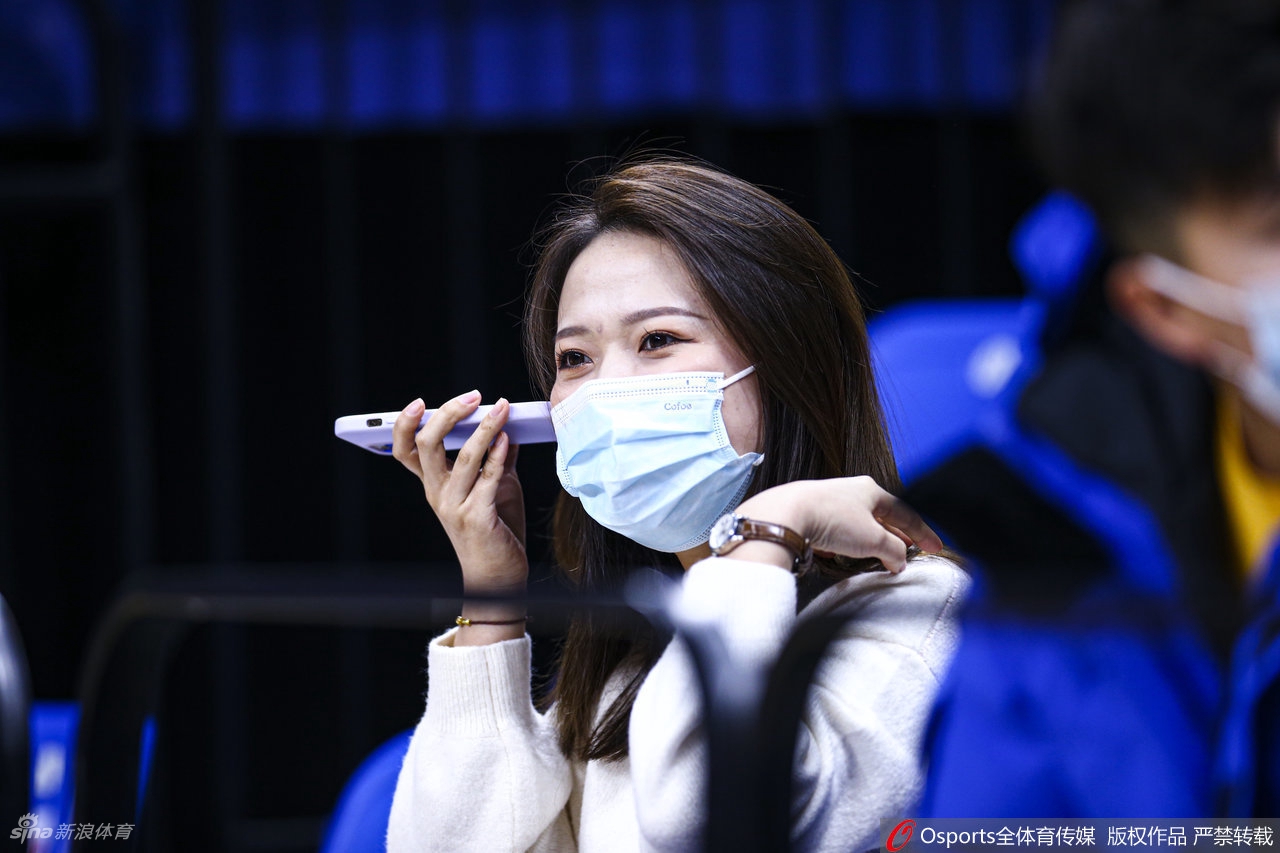 身穿白色外套的可爱女球迷，双手高高举起应援牌，眼中闪烁着兴奋的光芒，全然不顾周围人群的目光。