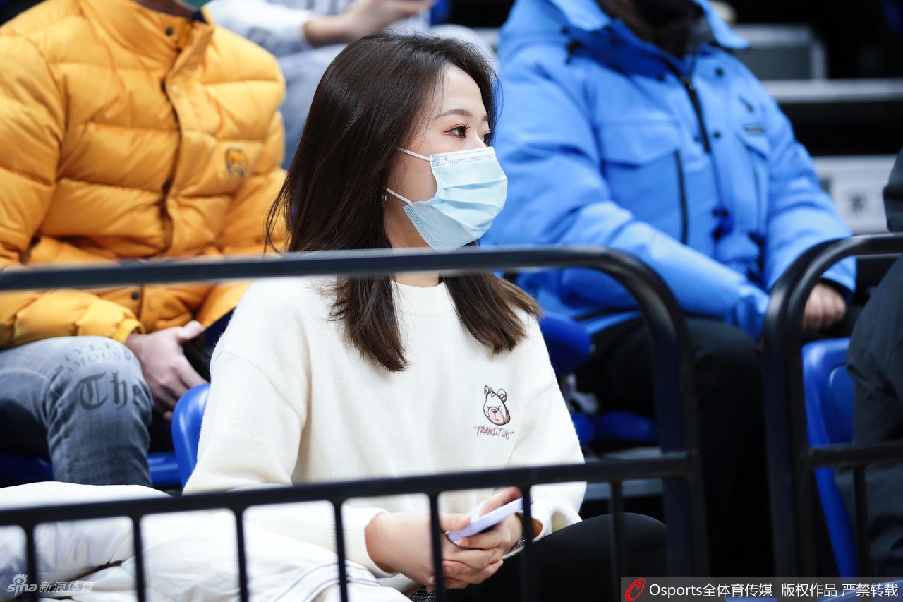 寒风中，一位穿着时尚运动装的短发女球迷，笑容灿烂地对着镜头比出胜利的手势，青春活力扑面而来。