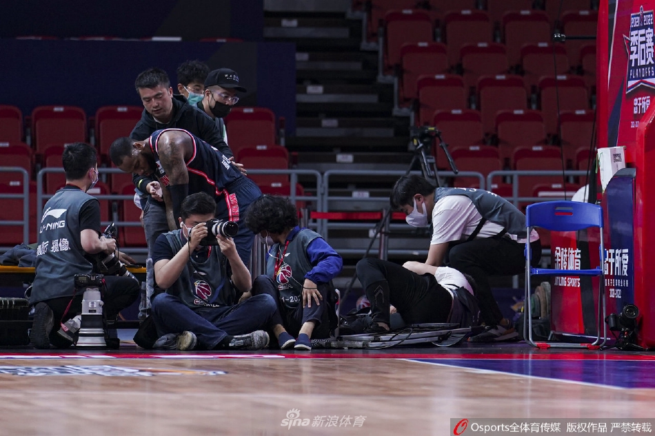 威姆斯重重地摔倒在杂乱的记者席中，扬起一片尘埃，他的身体深陷在座椅和设备之间，表情因剧烈的撞击而显得有些痛苦和茫然。