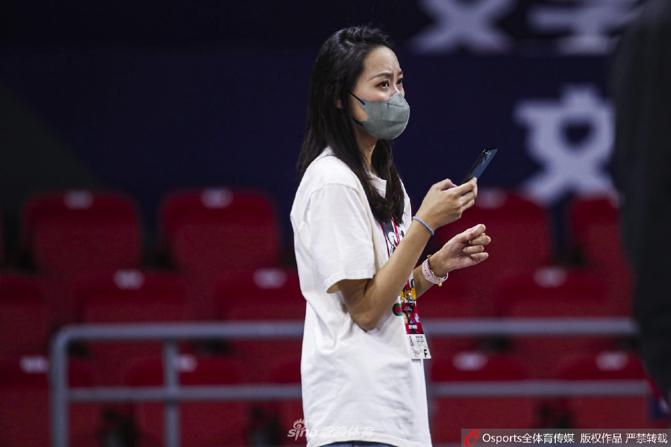 美女记者低头查看采访设备，乌黑的长发垂落肩头，她手指轻轻调试着录音笔，展现出职业女性在工作中的细腻与干练。