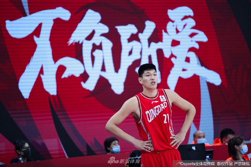 刘传兴在训练馆中进行拉伸放松，巨大的身形几乎占满整个镜头，他神情放松，但坚实的肌肉和修长的四肢依然透露出顶级运动员的强悍身体素质。