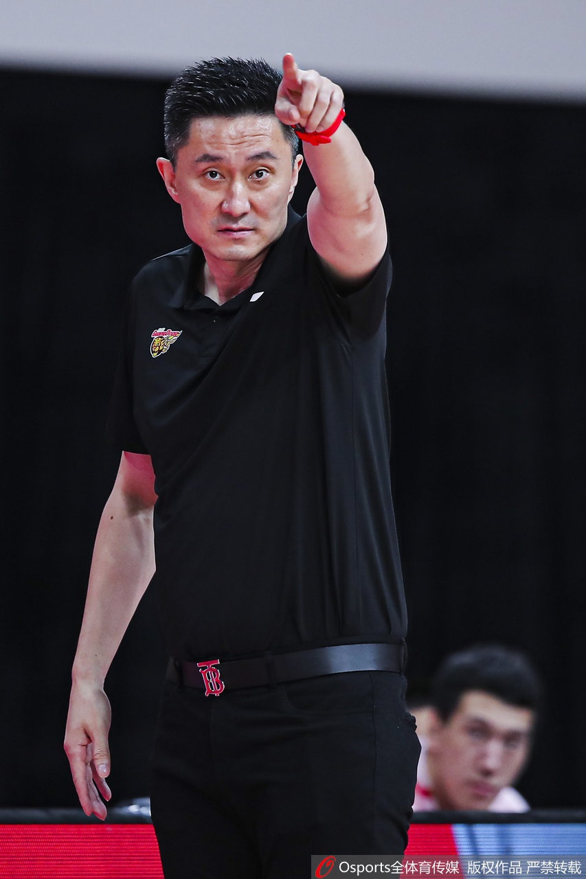 杜锋低头沉思,右手托着下巴,背景虚化的灯光衬托出他在喧嚣赛场中冷静布局的智帅风采