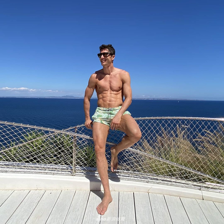 莱万身穿深色泳裤，侧身站在海边礁石上，他抬头望向远方，手臂上的肌肉线条因姿态而显得格外分明，胸肌和腹肌在侧光的照射下呈现出雕塑般的立体感，展现出无与伦比的男性魅力。