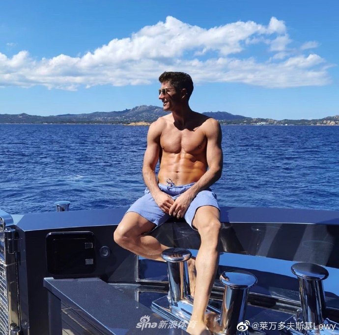 莱万多夫斯基赤裸上身站在清澈的海水中，他面带微笑，双手插在腰间，阳光洒在古铜色的肌肤上，勾勒出八块腹肌和清晰的人鱼线，宛如一尊古希腊雕塑。