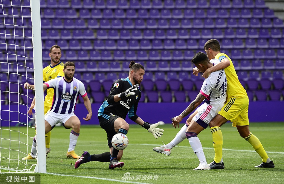 加的斯门将莱德斯马如雄鹰展翅般飞身跃起，指尖几乎触碰到飞速旋转的皮球，背景是巴拉多利德球员充满期待的眼神，攻防瞬间的张力在这一帧凝固