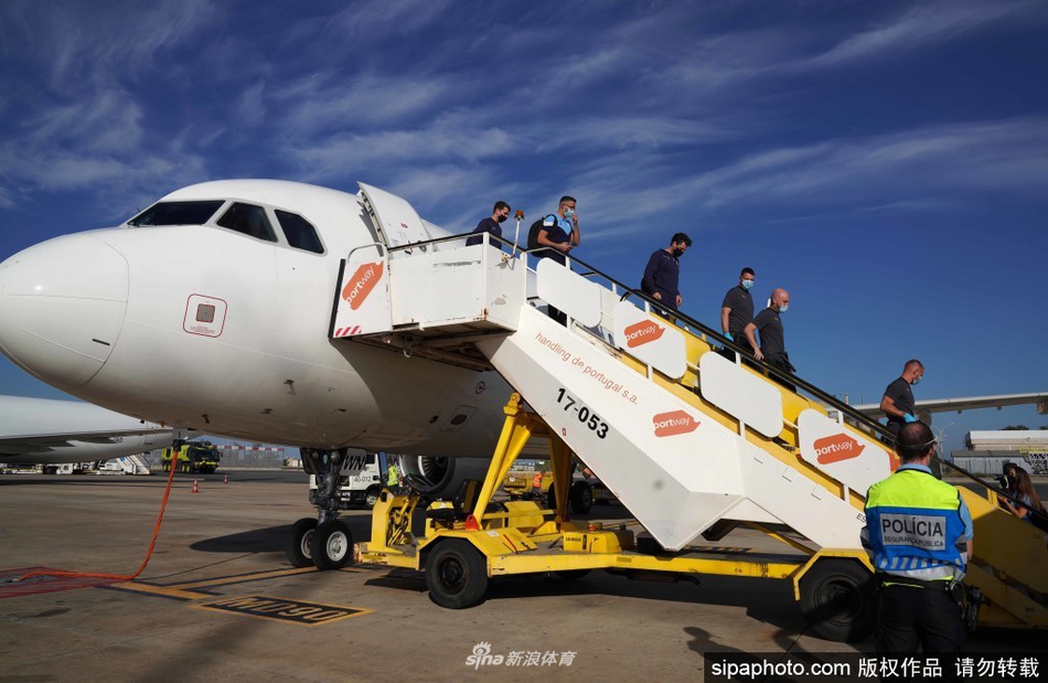 曼城将帅抵达里斯本机场，瓜迪奥拉身着休闲装神情专注，正与助手交流，背景是球队大巴，空气中弥漫着大战前的宁静与紧张。