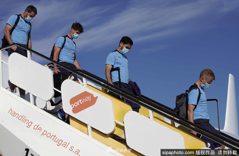 训练场上，核心德布劳内与斯特林进行传接球配合，两人面带笑容显得十分放松，身后的队友们正在进行抢圈游戏，背景是里斯本当地的特色植被。