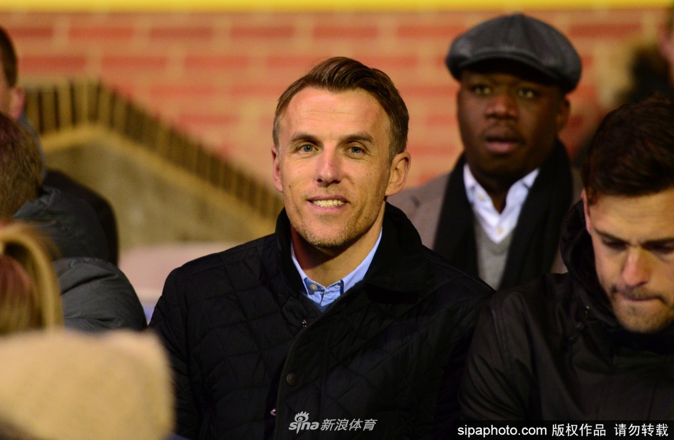 神情专注的菲尔-内维尔身着一丝不苟的深色西装，在聚光灯下凝视远方，胸前的迈阿密国际队徽熠熠生辉，仿佛预示着一段充满野心与挑战的新航程即将开启。