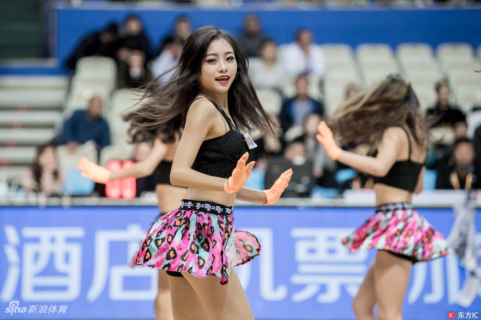 舞蹈进行到高潮部分，两名拉拉队员面对面热舞，她们的动作充满张力与默契，飞扬的发丝和自信的笑容在灯光下闪闪发光，展现出职业拉拉队的专业素养和青春活力。