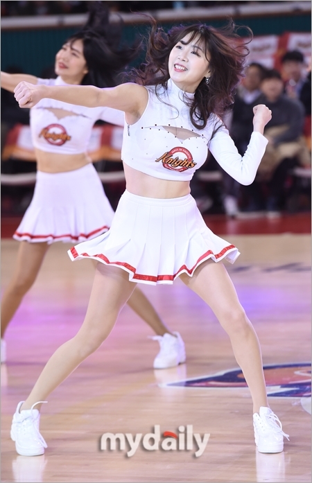 鏡頭捕捉到一位正專注熱舞的啦啦隊員,她身著黑色運動背心,露出健康的小麥色肌膚。隨著強烈的節奏甩動長髮,舉手投足間散發著青春陽光的活力與熱情。