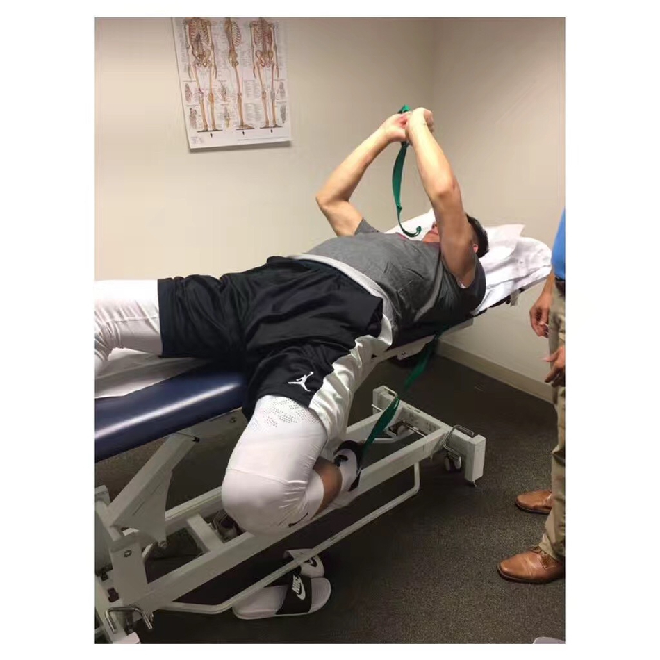 医生正在为可兰白克进行拉伸治疗，他紧咬牙关，小腿肌肉紧绷，虽然面容有些许痛苦，但依然全力配合着康复师的每一个动作。