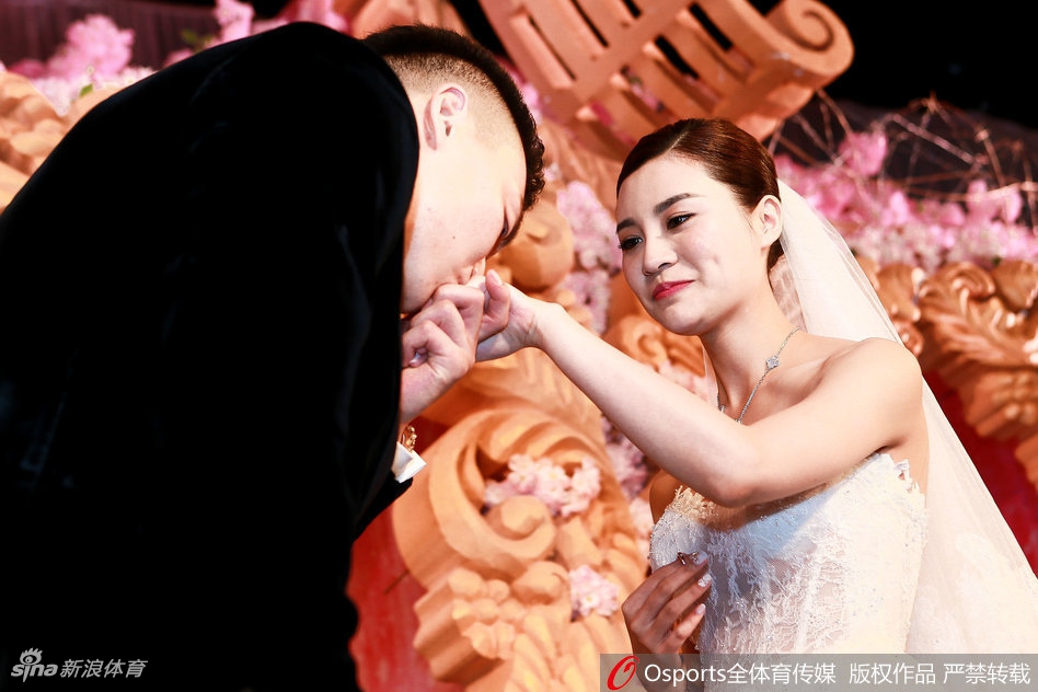 李根深情凝视身着洁白婚纱的妻子,他单膝跪地轻吻对方手背,无名指上的婚戒闪烁微光,身后是满座宾朋的祝福目光。