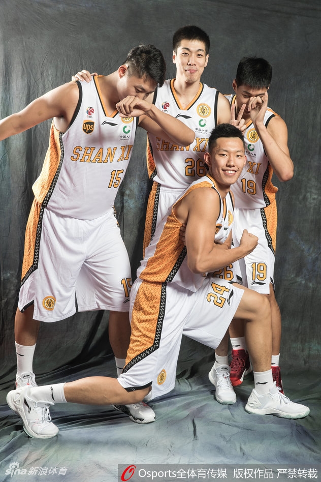 山西男篮队员在写真拍摄间隙互相搞怪打闹，一位队员正偷偷伸手拍向队友肩膀，表情狡黠，被抓拍的瞬间充满了欢乐的气氛。