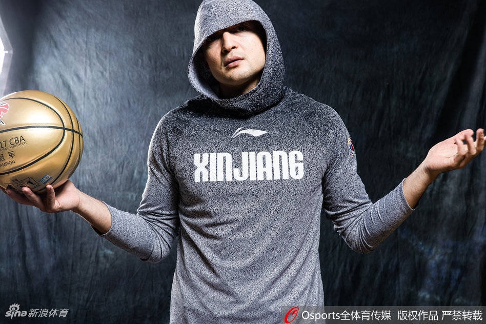 西热力江半身肖像,身穿浅色帽衫,头戴黑色毛线帽,身后是斑驳的墙壁,整体风格简约却极具嘻哈街头感