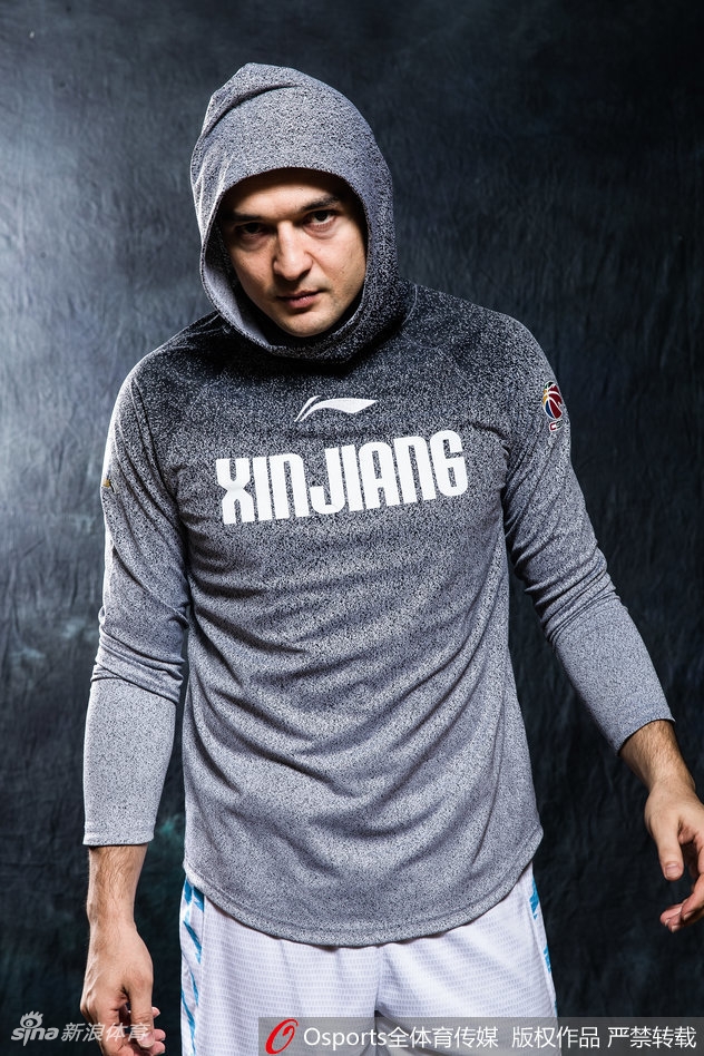 西热力江室内特写,暖光勾勒出他棱角分明的面庞,眼神坚定地望向一侧,背景虚化凸显出赛前的专注与宁静