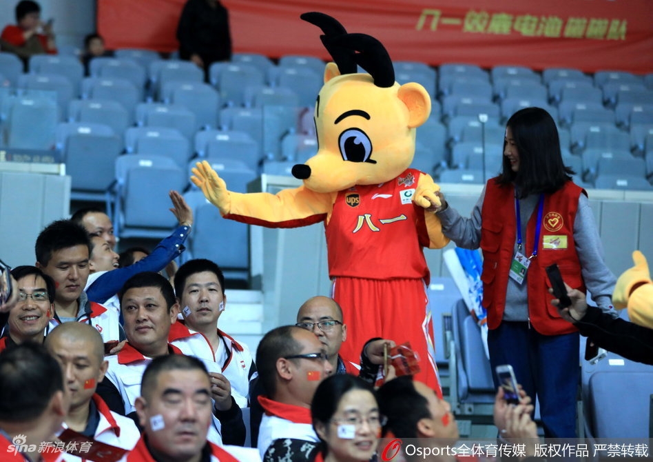八一火箭吉祥物张开双臂与看台前排的小球迷击掌,巨大的火箭头套在灯光下显得格外亮眼,孩子们兴奋地伸出小手,场面温馨又热闹