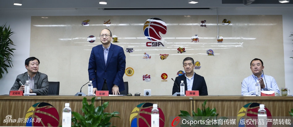 竞赛总经理张雄在话筒前神色严肃，手指轻点桌面，身后的大屏幕上显示着复杂的联赛数据图表，他正在向媒体详细解释裁判升降级制度的运行细则。