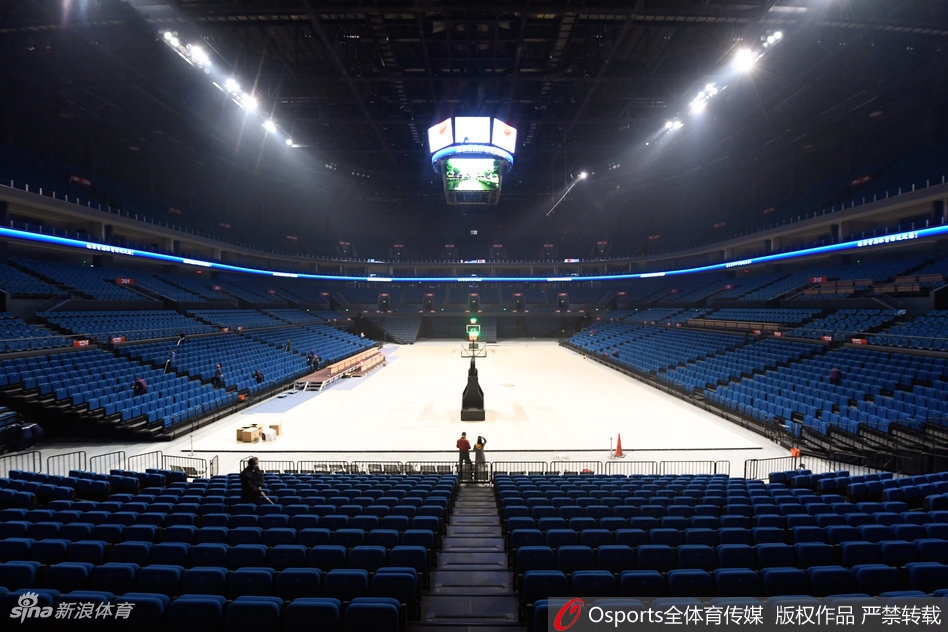 从高空俯瞰体育馆内部，巨大的中央漏斗屏正闪烁着红色的中国地图，四周看台上身着红色助威T恤的球迷座无虚席，汇成一片红色的海洋，场中央的球员正在灯光的聚焦下进行赛前热身。