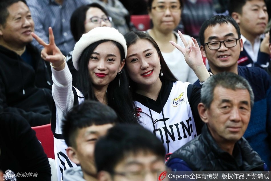 一位戴着眼镜、学生气质的辽宁美女球迷，高举着加油的手势，眼神坚定地望向赛场方向，全身心投入为辽篮助威。