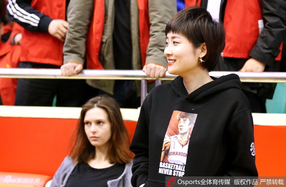 一位长发披肩的女球迷，在热闹的看台上展开一面印有“山东高速 丁彦雨航”的旗帜，神情专注而坚定