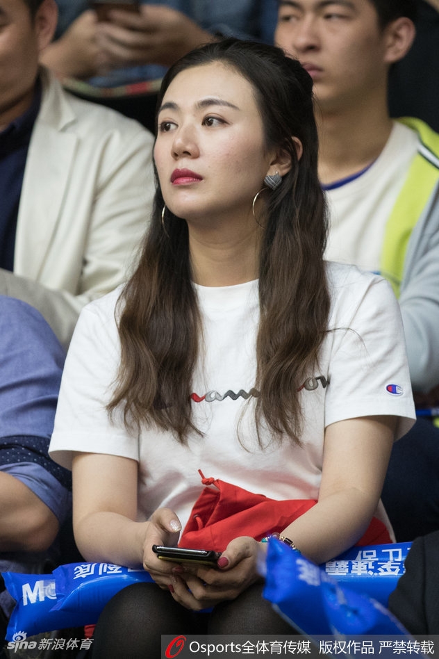 一位身穿白色上衣的广厦美女球迷在人群中格外抢眼，她带着浅浅的微笑为球队鼓掌，温柔的气质与赛场的热血形成动人对比。