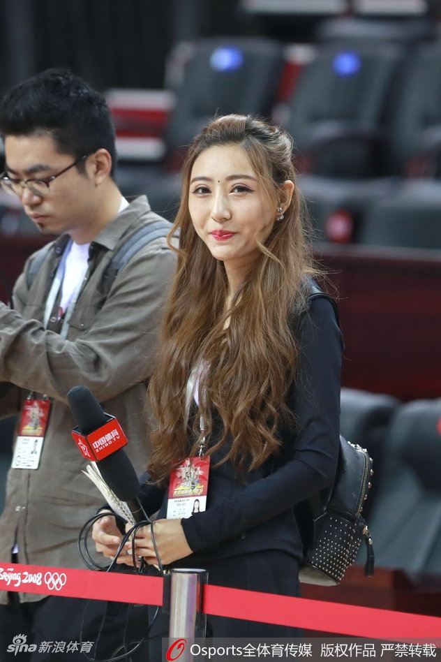 聚光灯下，美女主持人侧身回眸，眼神中充满了对比赛的专注与期待，背景是正在热身的辽宁队员，动静之间构成一幅生动的赛前画面。