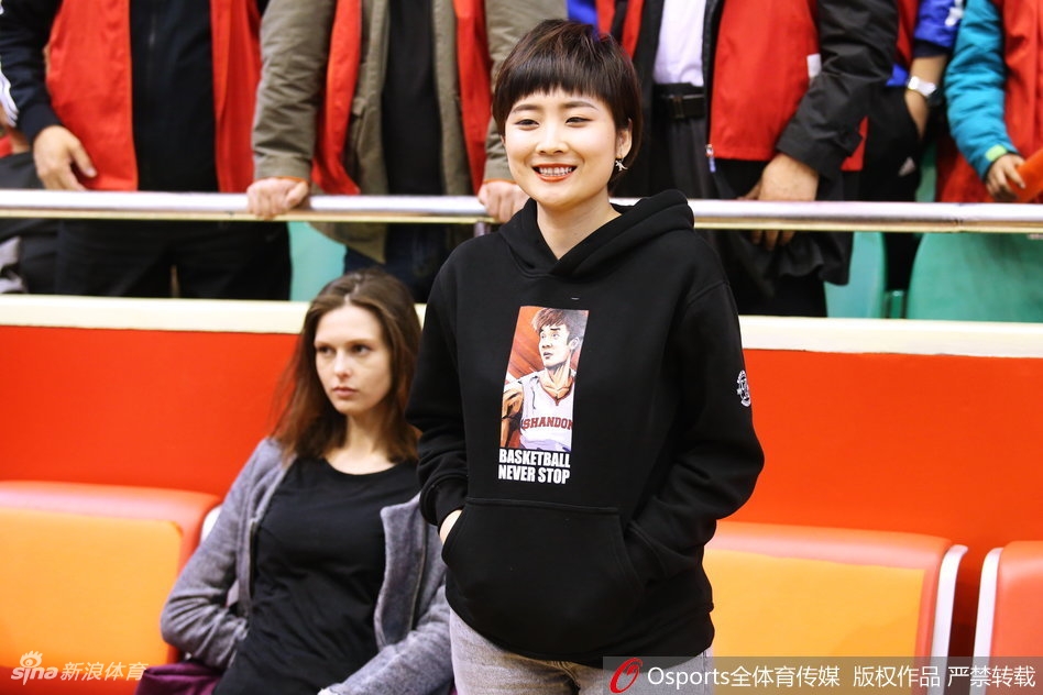 一位戴着眼镜的山东男球迷，身穿印有丁彦雨航卡通头像和“丁神”字样的白色卫衣，在全场沸腾的背景中露出会心的微笑