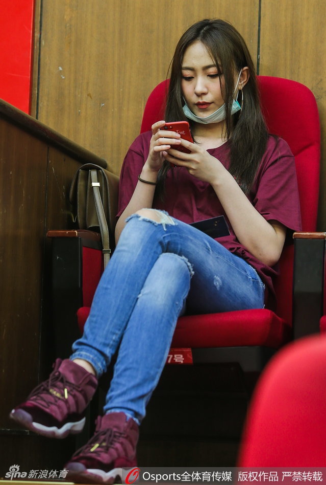 一位长发飘飘的广厦女粉丝身穿林志杰的球衣，双手握拳放在胸前，眼神专注地盯着赛场，为偶像默默祈祷