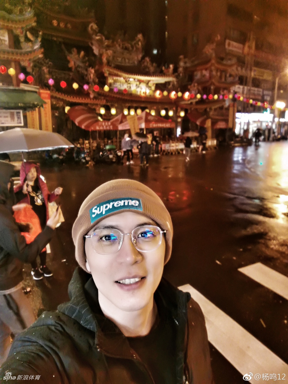 杨鸣与台北街头的特色招牌合影，面带微笑，心情极佳。背景中的繁体字广告牌和穿梭的人群，记录下这位CBA帅哥在宝岛留下的又一帅气瞬间。