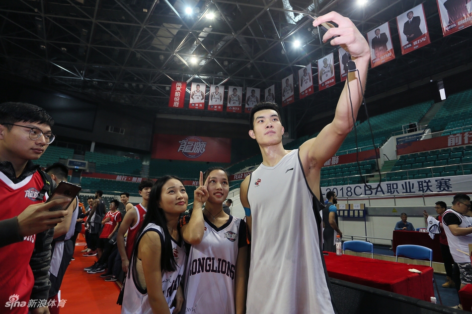 广州男篮的多名队员并排坐在场边长椅上,手中拿着签字笔,正在为身前排队的数十名球迷手中的纪念品签名,场面秩序井然。