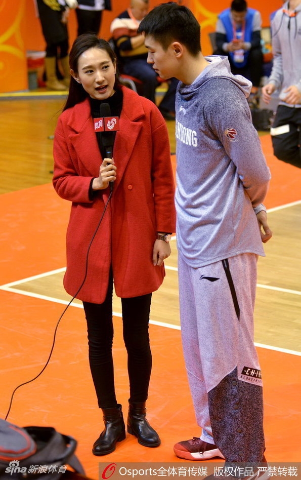 一位美女记者身着简约的灰色大衣,在球场通道内回眸一笑,她颈间挂着醒目的媒体证件,背景是略显模糊的球员通道,动静结合之间,仿佛凝固了赛前那一刻的紧张与期待。