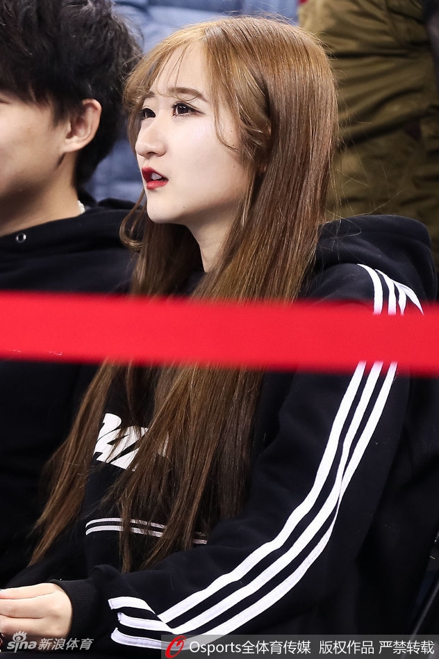 长发披肩的女生轻倚在栏杆旁，唇红齿白，眉眼间带着浅浅的笑意，她像是从画中走出的校园学姐，恰好路过这片热血沸腾的战场。