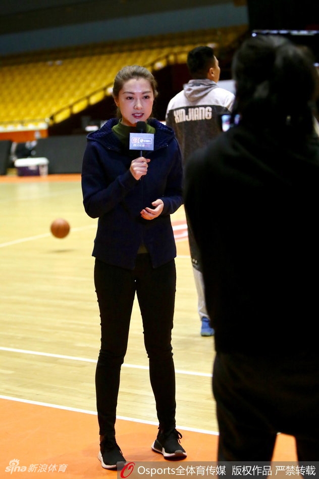 山东男篮的训练场上,一位高大的内线球员正持球背身单打,防守球员全力以赴,而在底线附近,美女记者半蹲着身子,以低角度抓拍着这次激烈的攻防对抗,神情极为投入。