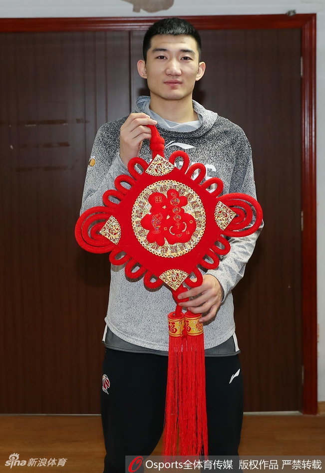 年轻球员展示春联时目光坚定，红色的纸张映衬着他青春的脸庞，寓意着广厦队的未来红红火火，充满希望。