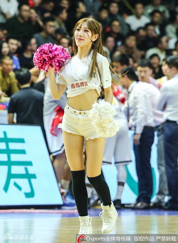 马尾辫啦啦队员回眸露出甜美微笑，背景中广厦球员正在热身，刚柔并济的画面定格了赛场内外的和谐共处。