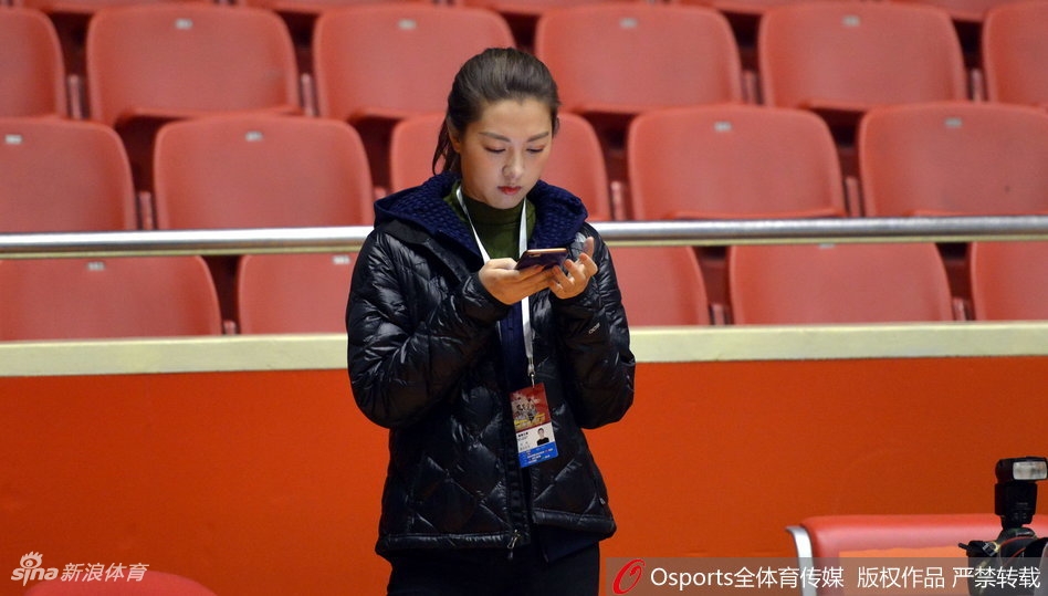 在明亮的训练场馆中,新疆男篮队员们正围绕教练认真聆听战术板上的布置,场边的美女记者手持笔记本,眼神专注地观察着球队的每一次合练细节,画面充满了备战的紧张感。