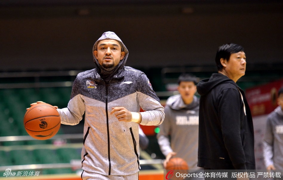 拉伸放松时刻，可兰白克坐在地板上，平静地望向远处，背景是空旷的球馆和队友模糊的身影，此刻的宁静预示着不久后即将在这里掀起的惊涛骇浪。