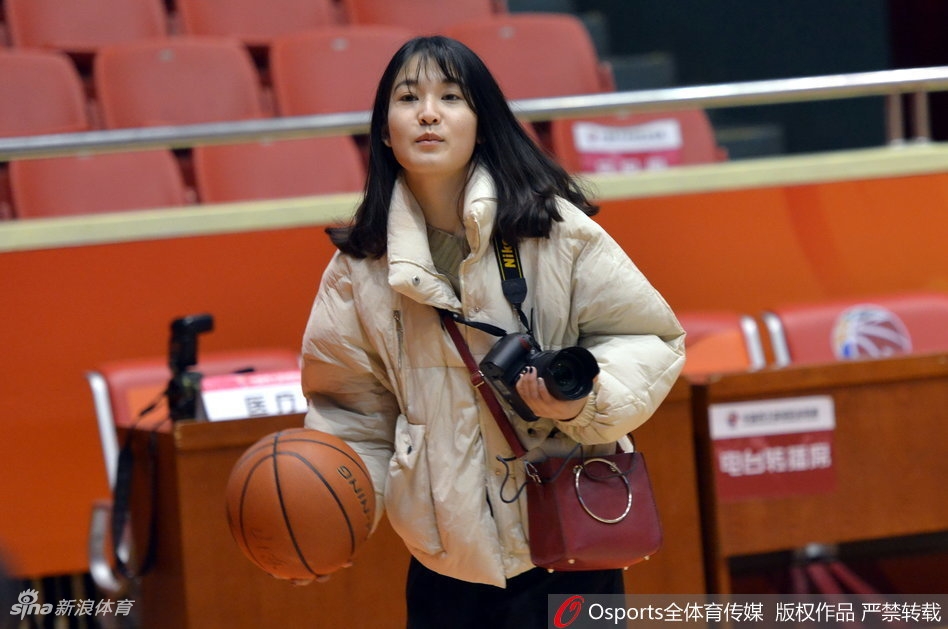 训练场全景,两边的篮架下分别摆放着新疆和山东队的训练用球。美女记者背对镜头,提着采访包正走向出口,整个球馆在灯光照射下显得格外庄重,一天的探营报道圆满结束。