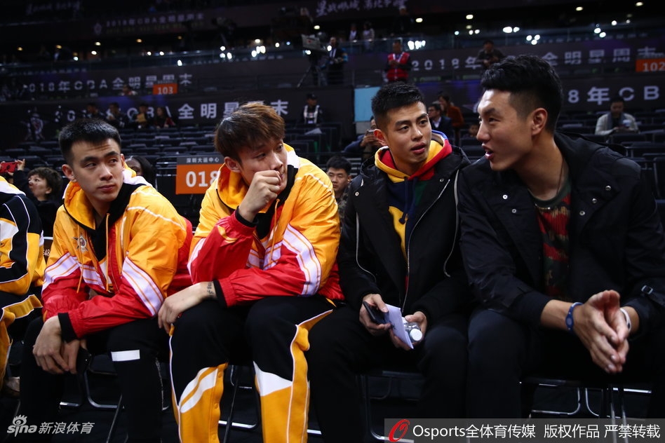 郭艾伦与方硕等北区全明星球员并肩坐在观众席上，郭艾伦手指场内，神情专注地与身旁队友交流着对比赛的看法。