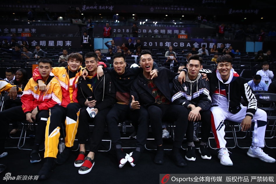 丁彦雨航与身旁的队友在观赛间隙神情放松地交谈，身后是座无虚席的深圳球迷，现场气氛热烈而轻松。