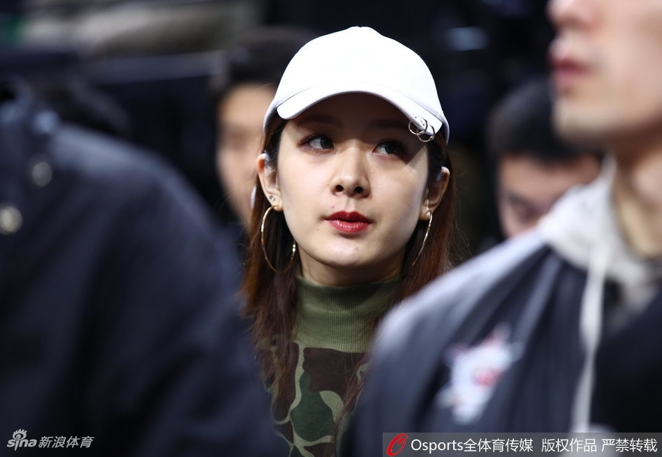 杨思雨在观众席上露出灿烂的笑容,眉眼弯弯,气质温婉大方。翟晓川则在一旁专注地看着她,眼神中充满爱意,背景是CBA全明星赛场的灯光与人群。