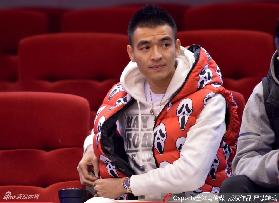 看台座位上,一位穿着时尚白色外套的年轻女球迷,手持橙色加油棒,侧身与同伴交谈,脸上洋溢着灿烂的笑容,仿佛对山东队的表现十分满意。