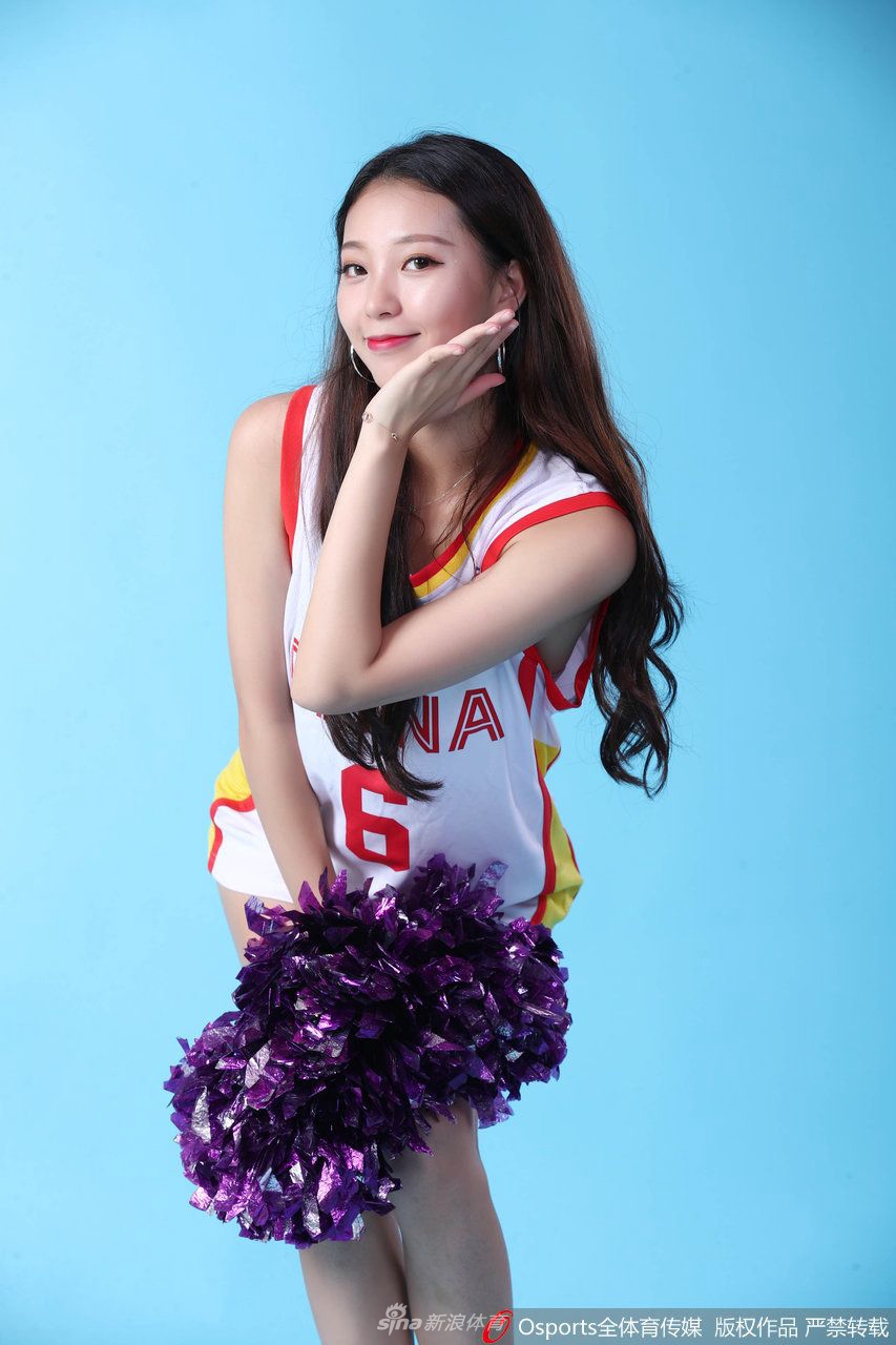 女孩坐在场边的广告牌上，双腿修长，姿态轻松惬意。她双手轻撑身体微微后仰，脸上的笑容既自信又温柔，仿佛刚刚完成训练，正在享受着赛前的片刻宁静。