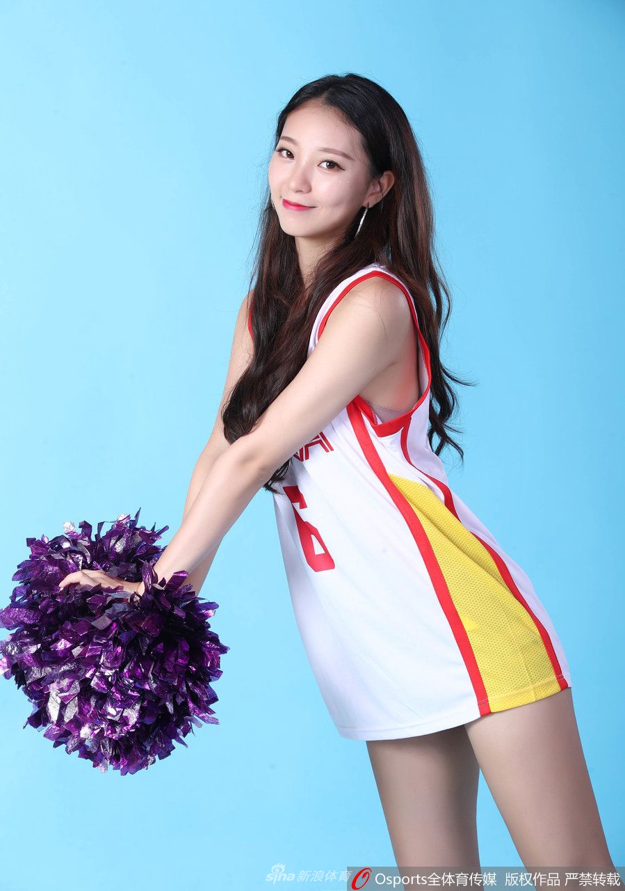 镜头近距离捕捉了一位戴着闪亮头饰的女孩，她肌肤胜雪，对着镜头甜美地眨眼，展现出篮球宝贝俏皮可爱的一面，背景虚化的球场灯光更衬托出她的光彩照人。